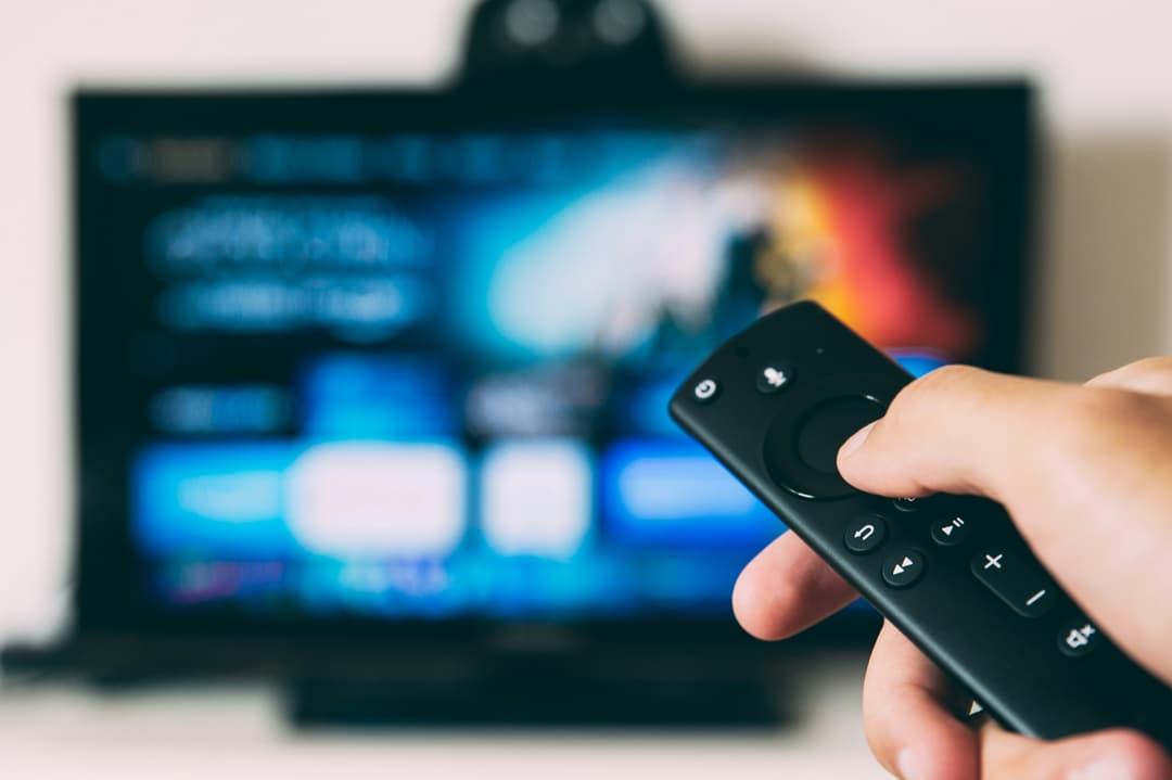 O telecomandă ținută în mână și un televizor în fundal